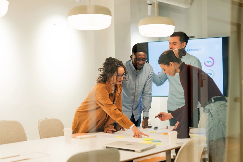 Four young professionals are working together in a modern office, analyzing data and planning a new strategy using sticky notes on a large table