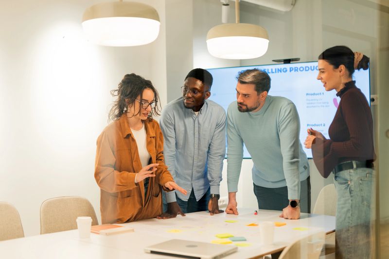 Four young colleagues are discussing new ideas for selling products, analyzing data and developing new strategies during a business meeting in a modern office