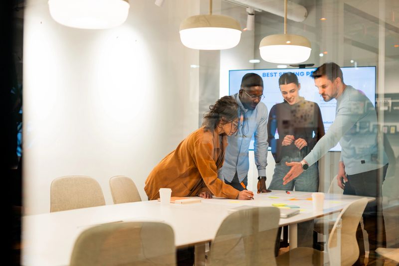 Four marketing specialists collaborating on a new strategy, engaging with a whiteboard and sticky notes in a modern office setting, fostering teamwork and innovative ideas