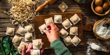 Hands preparing ravioli on a wooden board.