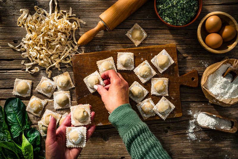 Italian food: Woman's hansd arranging homemade Ravioli and tagliatelle on a table