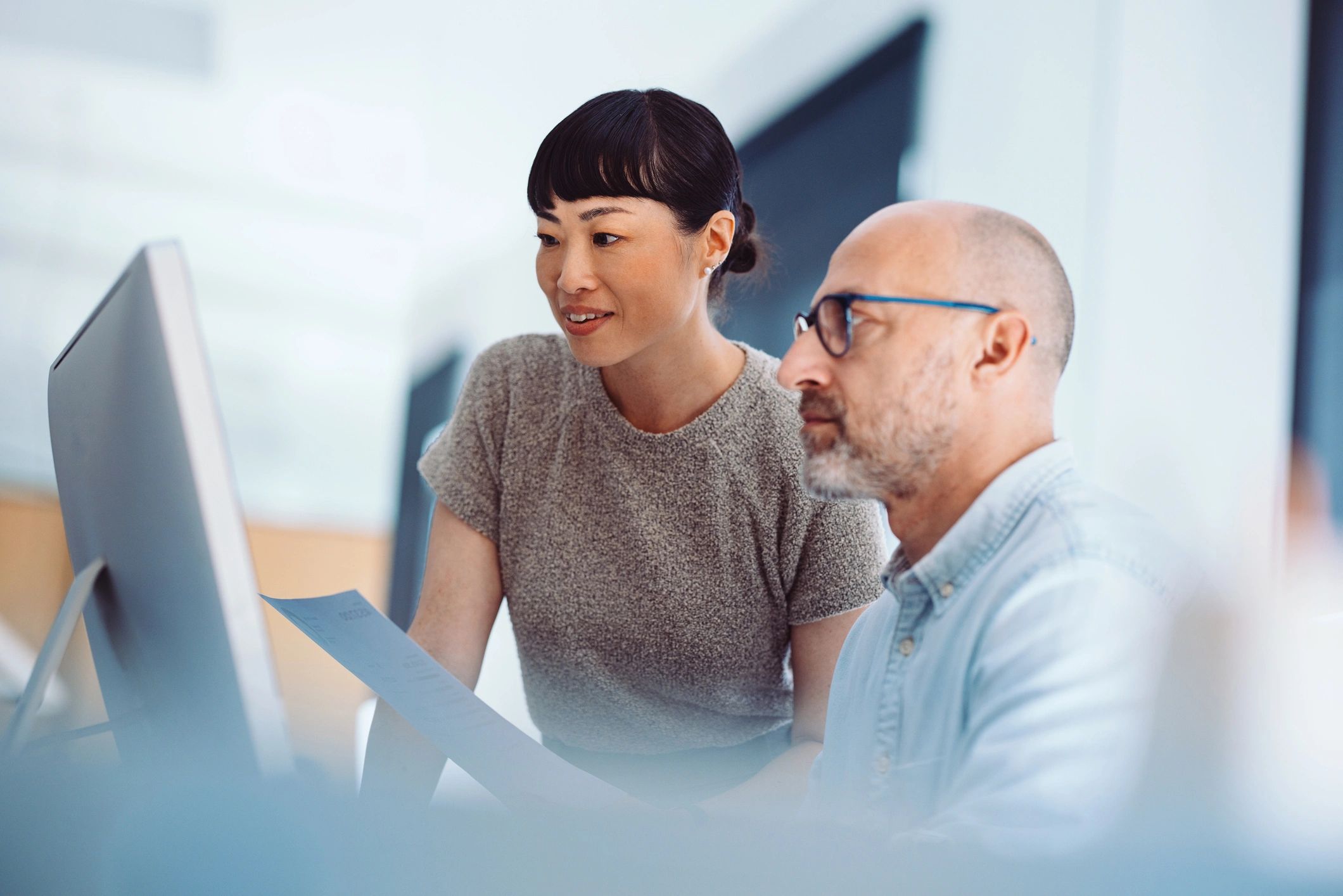 Two colleagues collaborating at a computer in an office setting.