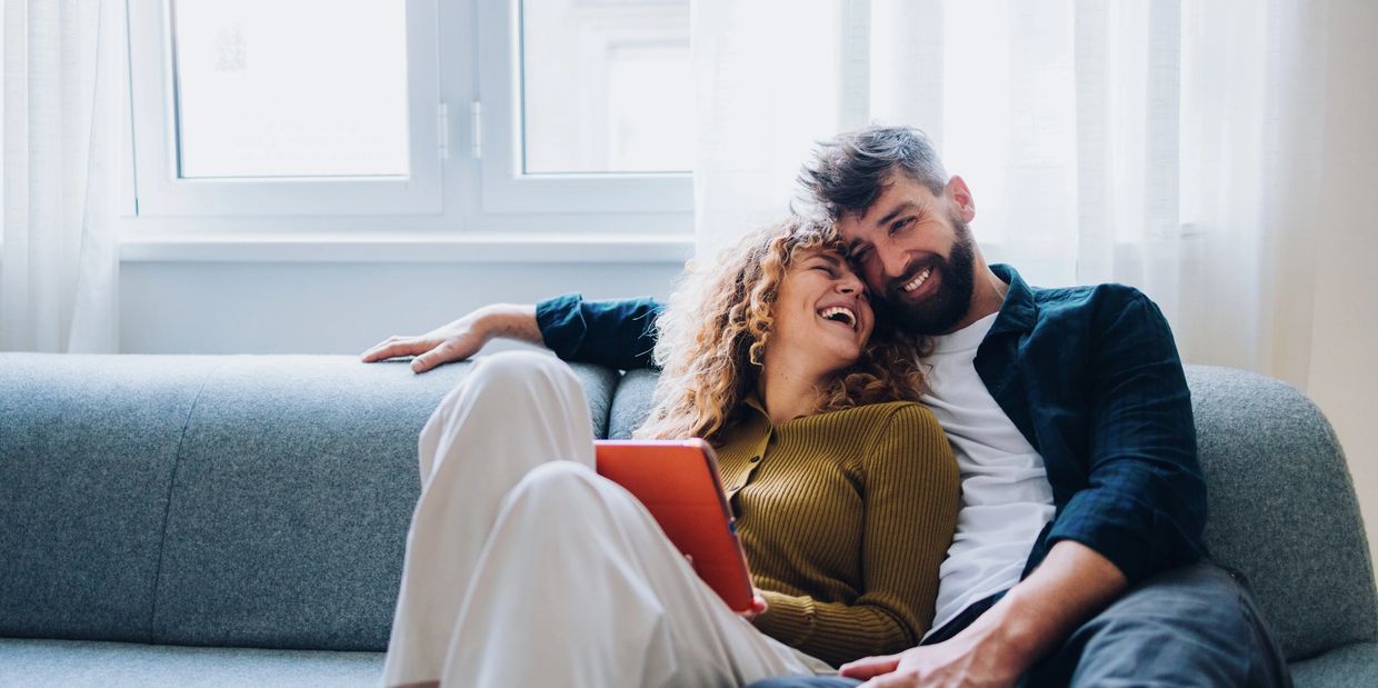 A happy couple laughing together on a couch in a bright room.