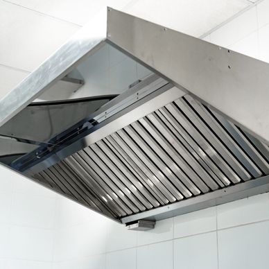 A stainless steel commercial kitchen exhaust hood mounted on a tiled wall.