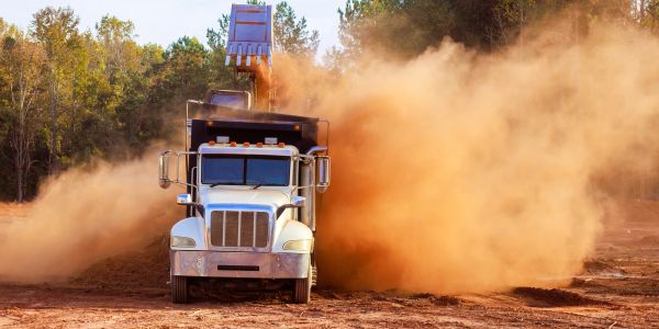 Dump truck releasing dirt on soil ground.