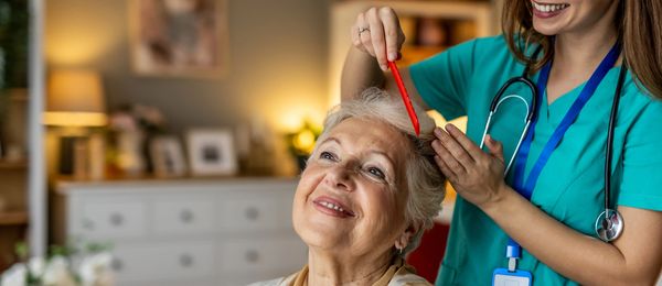 A nurse combing an elderly woman's hair with care and a smile.
