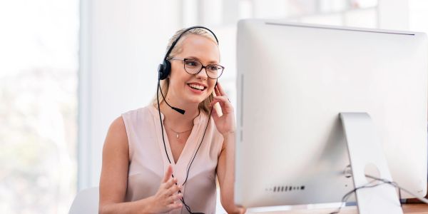 Smiling woman with headset working on a computer.