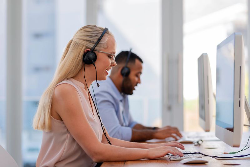 Two customer service representatives wearing headsets work attentively at modern computer workstations, showcasing professionalism and teamwork, in a bright and stylish office environment.