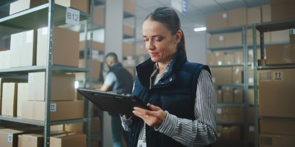 Woman using a tablet in a warehouse filled with boxes.