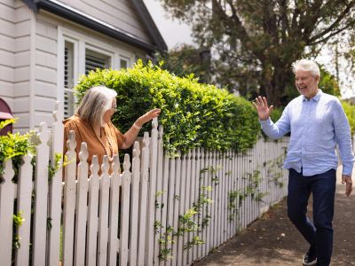 Neighbors greeting each other over a white picket fence.