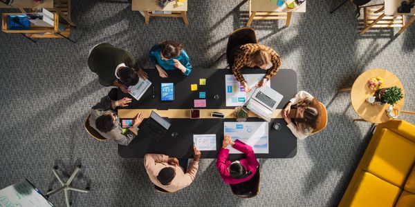 A diverse group collaborating around a table with laptops and charts in a modern office.