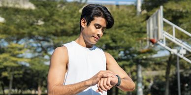 Young man in white sleeveless shirt checking his smartwatch outdoors.