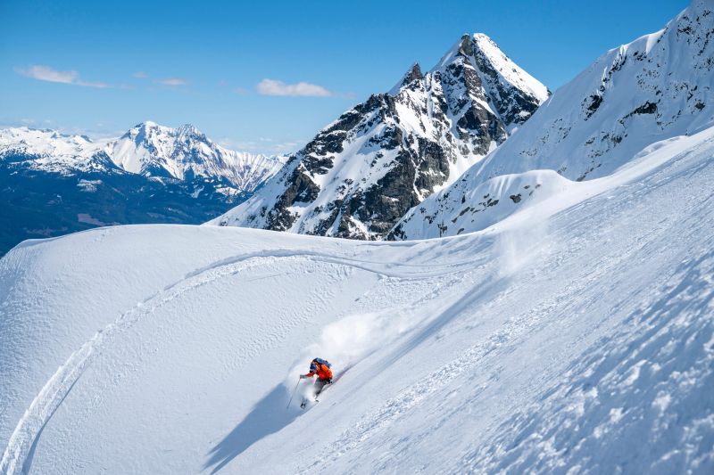 Backcountry skier descends mountain top through fresh powder snow, Tantalus Range, B.C.