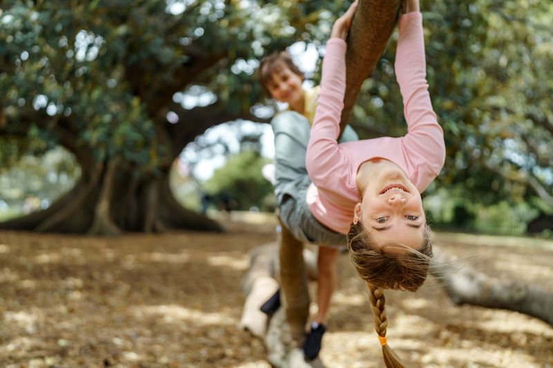 Girl posing for camera while hanging upside down on a tree branch