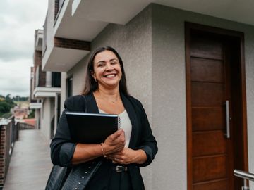 Smiling woman holding notebook outside modern building.