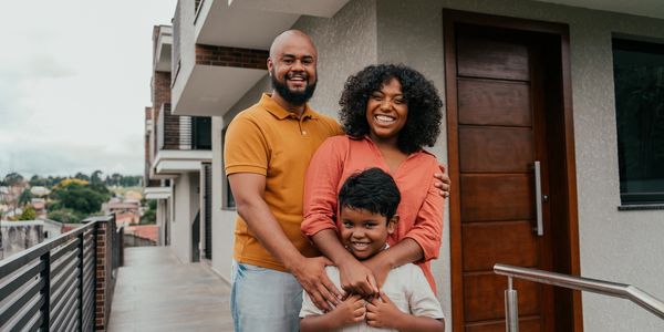 Happy family standing together outside their modern home, smiling warmly.