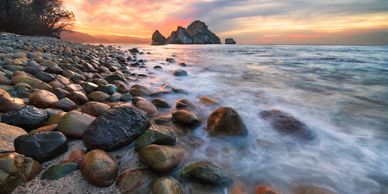 Rocky shoreline at sunset with waves gently washing over stones.