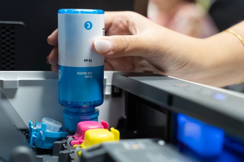 Hand holding ink bottle. Refill ink tank for ink jet Printer. Employees refilling ink into a ink tank printer at home office. Hand holding blue ink cartridge and insert to the printer.