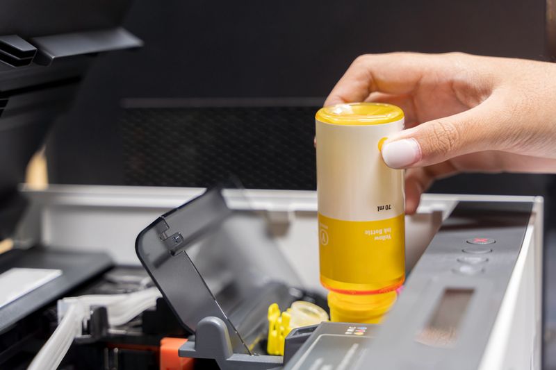 Refill ink tank printer at office. Close up printer cartridge inkjet of color yellow CMYK and repair fix the problem concept , selective focus