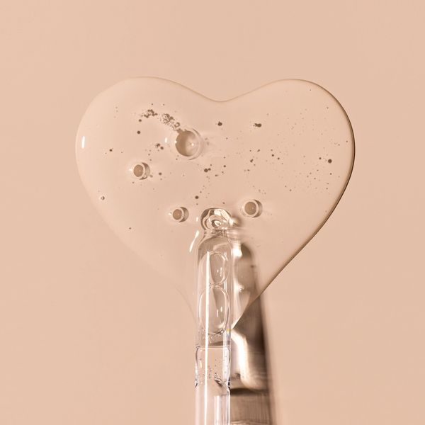 Clear serum drop shaped like a heart on a beige background.