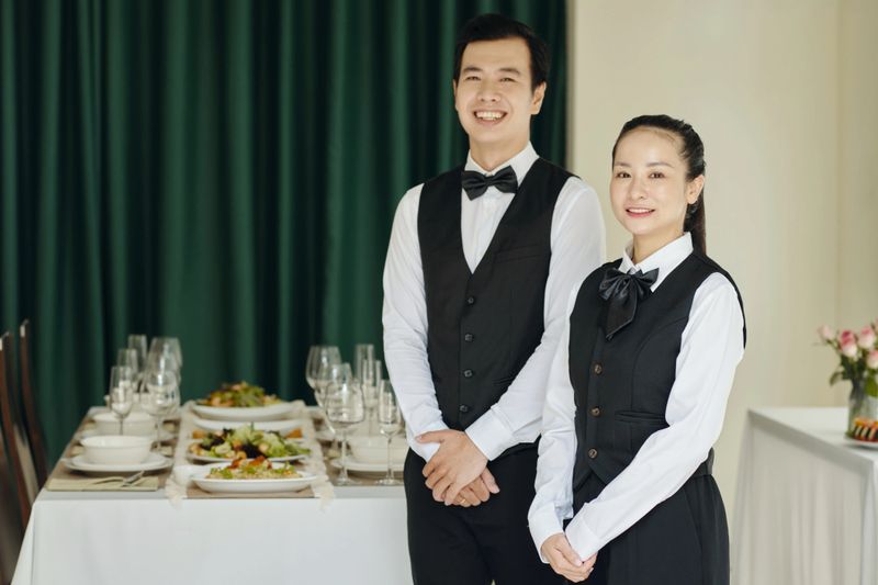 Portrait of waitstaff smiling at camera while setting up dinner service in an elegant dining area