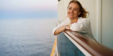 Woman smiling on a cruise ship balcony at sunset.