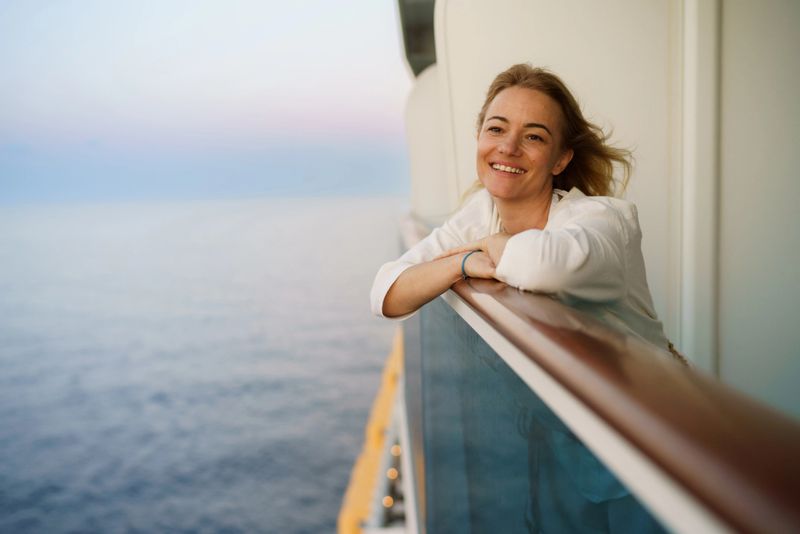 A smiling woman on the balcony of a cruise ship looks into the distance
