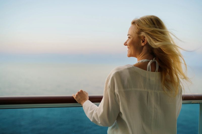 Rear view of a happy woman with blond hair is enjoying on the terrace of a cruise ship and looking into the distance