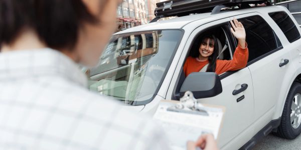 Woman waves from car to driving instructor.