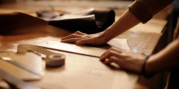 Hands working with leather and measuring tools on a wooden table.