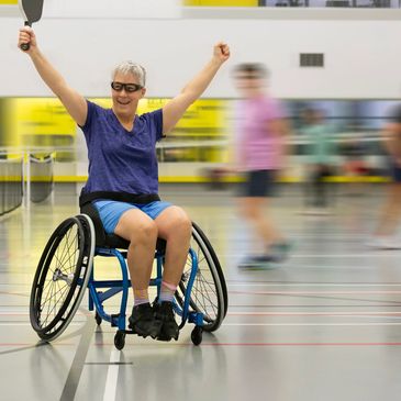 Happy woman in wheelchair playing pickleball.