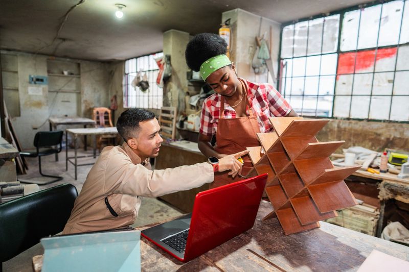Carpenter showing woodshelf to coworker on a woodshop