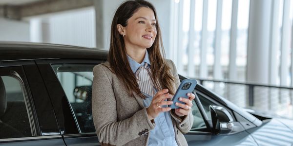 A woman standing by her car using a smartphone with a smile.