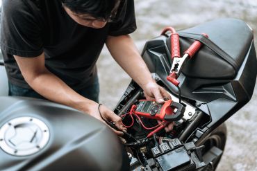 Person using a multimeter to check a motorcycle's battery.
