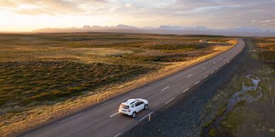A white car driving on an open road through a vast landscape at sunset.