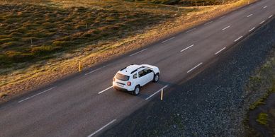 A white car driving on a rural road during sunset.