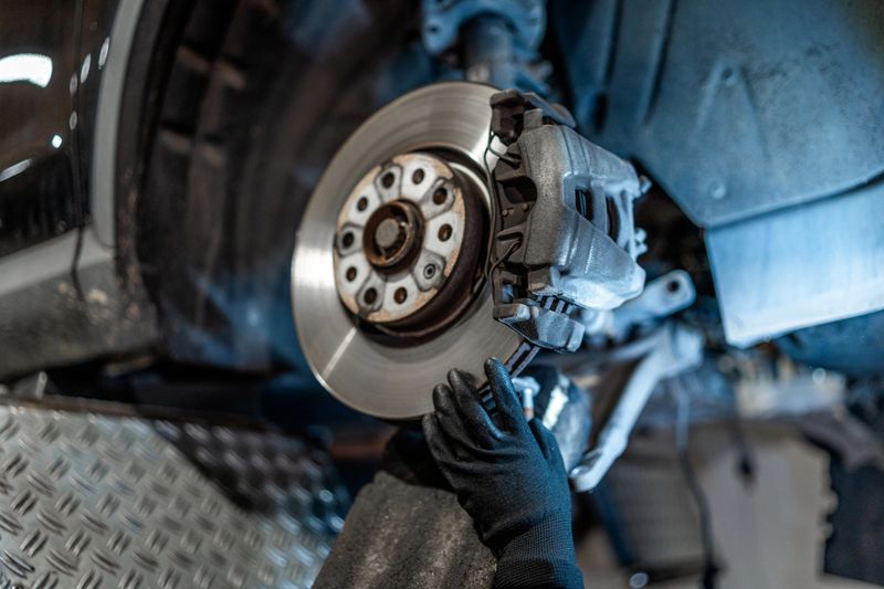 Close up of mechanic's hands wearing gloves, inspecting car brake disc and caliper during maintenance in auto repair shop