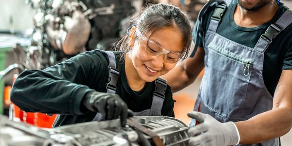 young girl being assisted working on a transmission in a shop with a man next to her teaching her