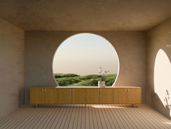 Minimalist room with a wooden cabinet and circular window overlooking grassy hills.