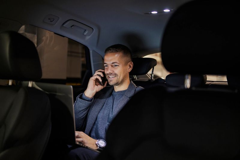 Smiling busy executive on backseat in a car is having phone conversation and working on a laptop.