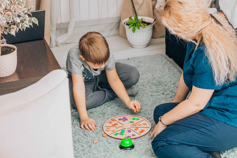 Little boy concentrating on an interactive learning activity with a teacher in a comfortable educational space, highlighting the importance of play-based therapy and child psychology