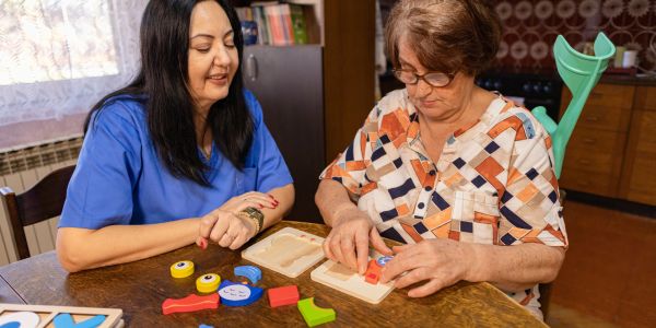 Two women working on a wooden puzzle at a table.