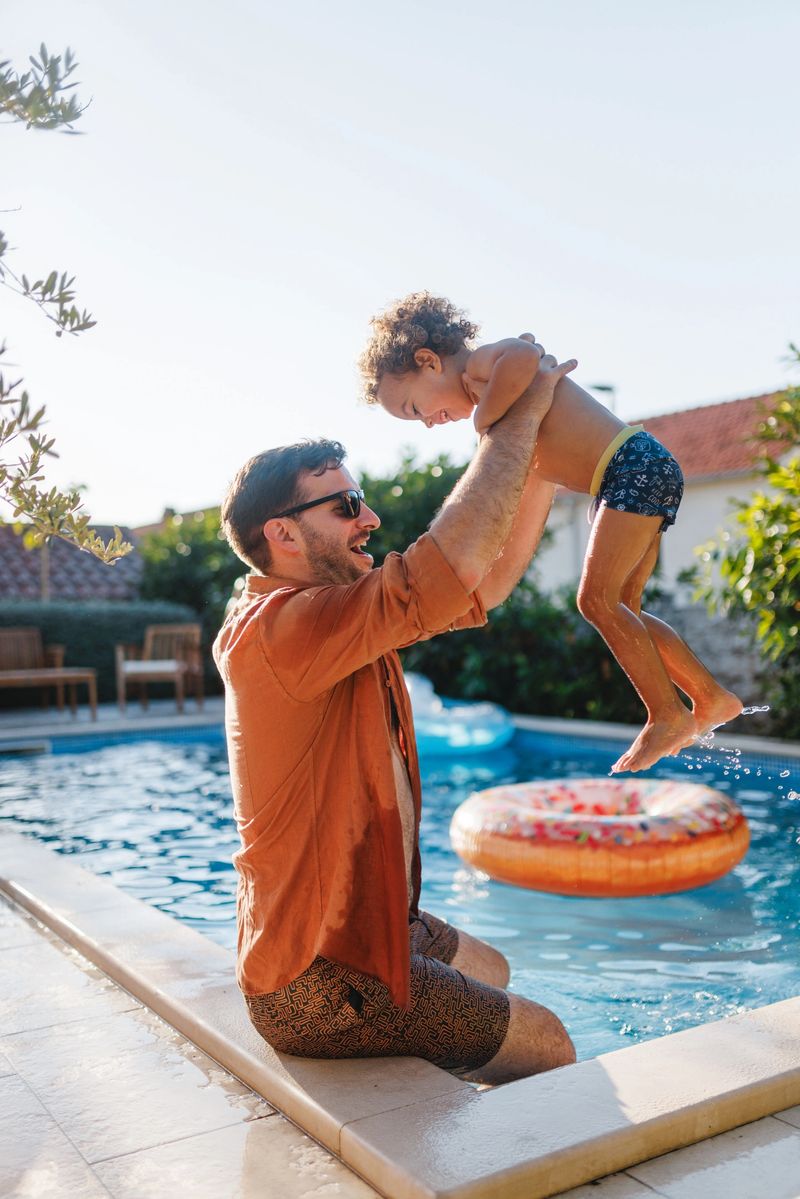 A joyful moment between a father and his young son by the pool, capturing carefree bonding and vacation fun. The image reflects happiness, togetherness, and love in a beautiful outdoor setting on a sunny day.