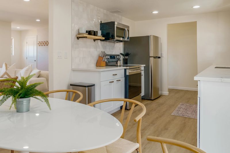Modern, bright interior kitchen with white cabinetry, and a light wood floor. Dining table with wicker wood chairs.