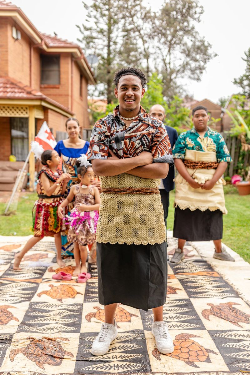 A Tongan family gathers in their Sydney backyard, dressed in vibrant traditional attire. They celebrate their culture, sharing joy and unity while showcasing indigenous lifestyle.