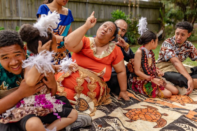 In a lively gathering in Sydney, a Tongan family engages in conversations, wearing traditional clothing, celebrating their cultural heritage with warmth and unity.