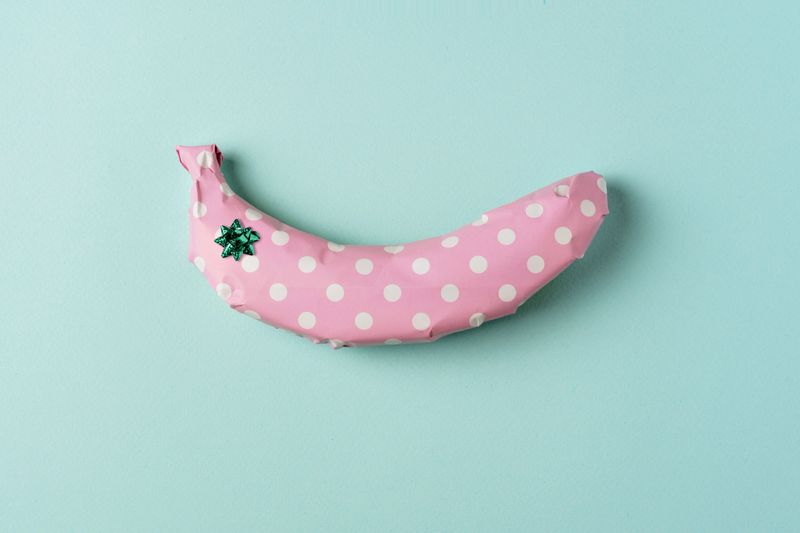 Banana wrapped in pink polka dot gift paper with small green bow on pastel blue background, creating playful and creative composition.