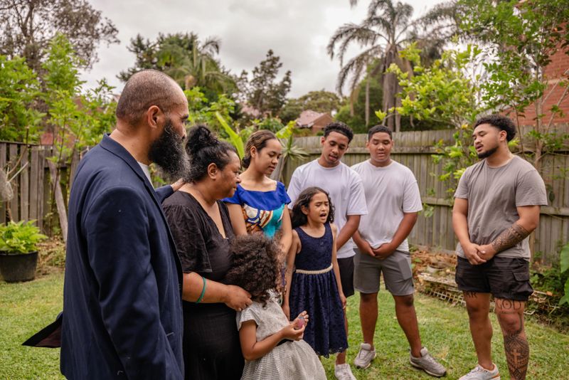 A Tonga family gathers in their backyard in Sydney, Australia, sharing moments of joy and connection. Lively conversations and smiles reflect their rich cultural traditions.