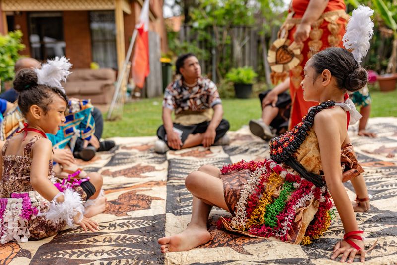 A Tongan family gathers in Sydney, Australia, celebrating their cultural heritage through lively interactions and traditional attire, creating a warm atmosphere filled with happiness.