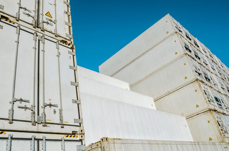 Tall stacks of white refrigerated cargo containers against a clear blue sky